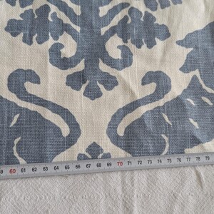 May include: A close-up of a white fabric with a blue patterned design. The pattern features stylized swans and leaves. A ruler is placed on the fabric, showing measurements in inches.