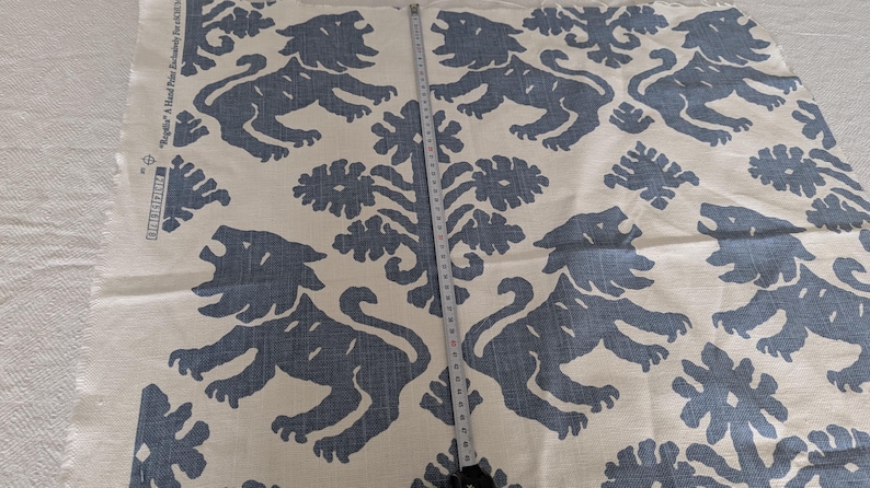 May include: White fabric with a repeating pattern of blue stylized lions and floral designs. The fabric has the text "Ragazzi - A Hand Printed Fabric Exclusively for..." printed on the side.