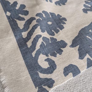 May include: Close-up of a white fabric with a blue floral pattern. The fabric has a textured surface and a frayed edge.