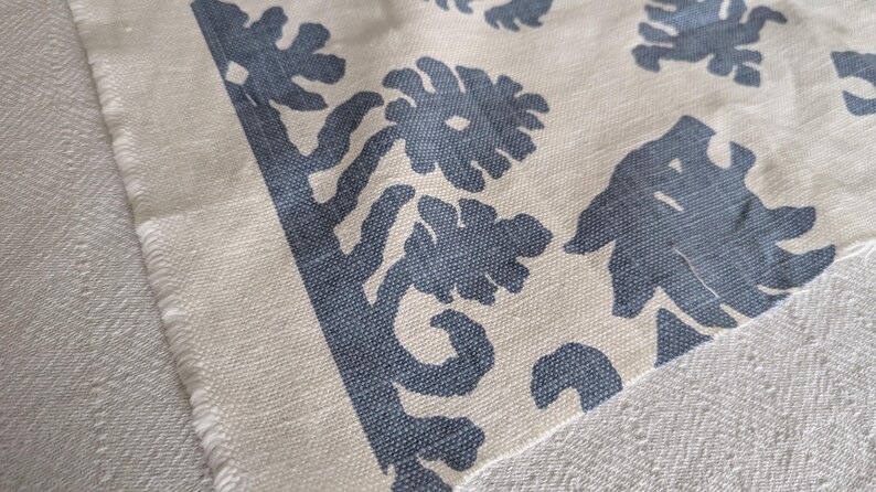 May include: Close-up of a white fabric with a blue floral pattern. The fabric has a textured surface and a frayed edge.