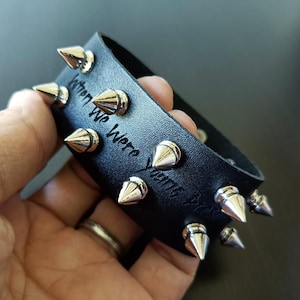 May include: Black leather bracelet with silver-colored cone studs. The bracelet has the words "When We Were Young" engraved on it. A stylish accessory.