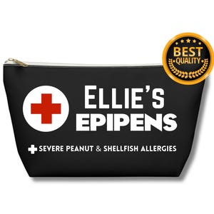 Può includere: Borsa nera con cerniera con una croce bianca e il testo "Ellie's Epipens" in bianco. Sotto il testo c'è un segno più bianco e il testo "Allergie gravi a arachidi e frutti di mare" in bianco.
