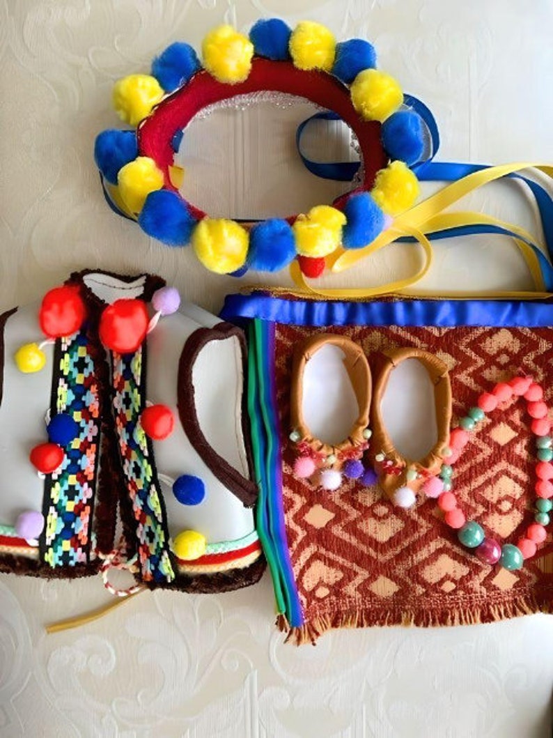 May include: A set of traditional Ukrainian folk costume accessories, including a headband with yellow and blue pom-poms, a white vest with colorful embroidery, a pair of brown leather slippers with pom-poms, and a red and brown bag with a colorful patterned fabric.