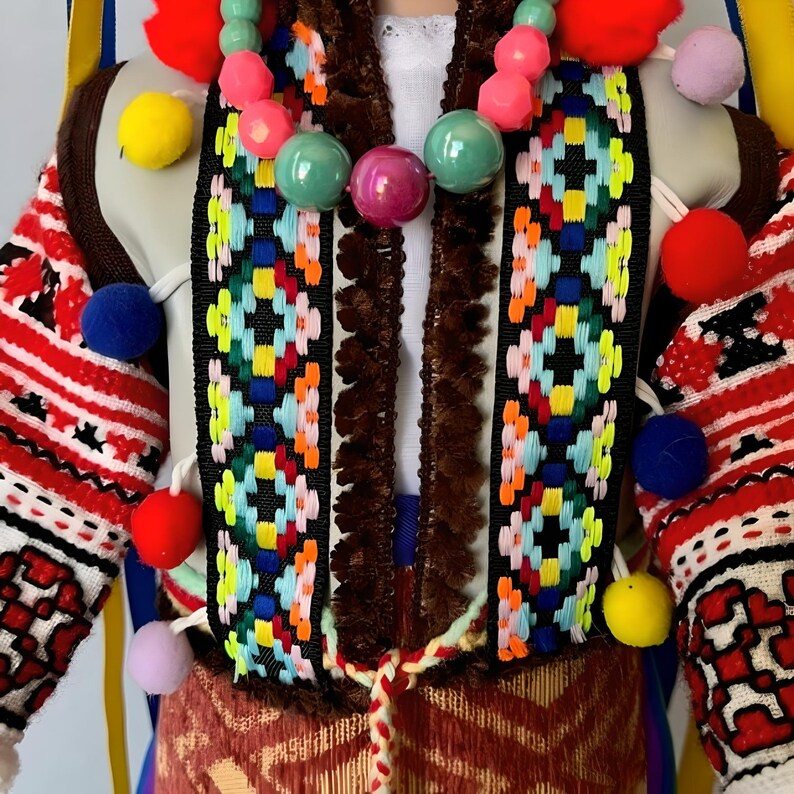 May include: A colorful folk costume with a red, white, and blue embroidered pattern. The costume features a brown fur trim, a multi-colored beaded necklace, and pom-poms in various colors.
