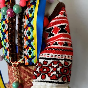 May include: A red, white, and black embroidered sleeve with a geometric pattern. The sleeve is part of a traditional folk costume.