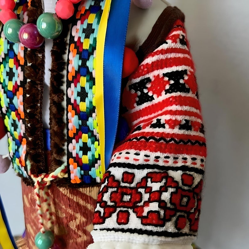 May include: A red, white, and black embroidered sleeve with a geometric pattern. The sleeve is part of a traditional folk costume.