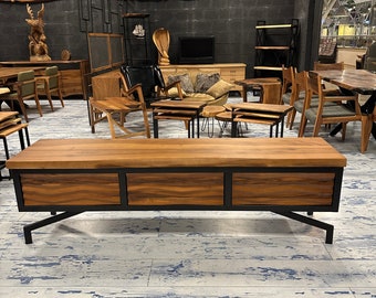 Puede incluir: Una mesa de centro de madera con tres cajones y patas de metal negro. La mesa tiene un acabado de madera natural y está sobre un suelo de madera blanqueada.