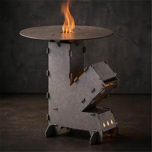 Puede incluir: Una mesa de fogata de metal gris oscuro con una parte superior redonda y una abertura central para las llamas. Las llamas son de color naranja y amarillo. La mesa tiene un diseño geométrico con juntas visibles y una base robusta.