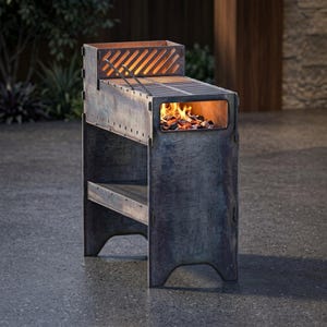 May include: A rectangular metal grill with a weathered dark gray finish, featuring a top cooking grate, a side firebox opening with glowing orange embers, and a lower storage shelf. The structure is composed of interlocking panels with visible seams.