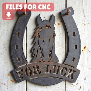 May include: A dark gray metal wall art piece shaped like a horseshoe with a horse head silhouette in the center and the text FOR LUCK cut out at the bottom. The metal has a weathered, textured finish and is mounted with two visible nails.