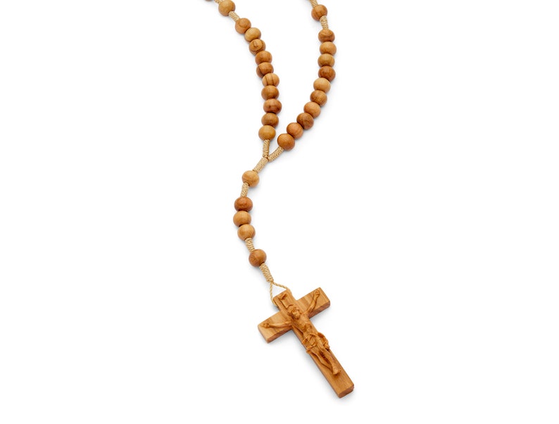 Puede incluir: Un rosario de madera con un crucifijo que presenta una figura tallada de Jesucristo. Las cuentas son marrones y la cuerda es beige.