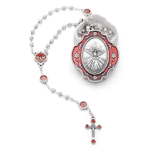 May include: A silver rosary with red detailing. The rosary includes a crucifix, decorative beads, and a pendant with a dove design. The rosary is shown with a white container with a red framed pendant.