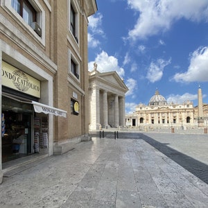 Puede incluir: Una vista de la Plaza de San Pedro en la Ciudad del Vaticano, Roma, Italia. La plaza est&aacute; vac&iacute;a, con solo unas pocas personas caminando. En el fondo, la Bas&iacute;lica de San Pedro es visible, con su ic&oacute;nica c&uacute;pula y fachada. La plaza est&aacute; rodeada por una columnata de columnas, que crean una sensaci&oacute;n de grandeza y escala.