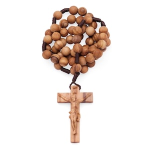 May include: A rosary featuring round, light brown wooden beads with visible grain patterns, strung together with dark brown cord. The rosary terminates in a wooden crucifix that displays a carved figure of Jesus Christ centered on the cross.