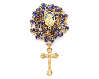 May include: A gold-colored rosary with blue beads. The rosary features a gold crucifix and a centerpiece with an image of the Virgin Mary. The beads are a deep blue color and are connected by gold-colored chain.