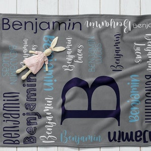 May include: A gray fleece baby blanket with the name "Benjamin" repeated in a variety of fonts and colors. The blanket also features a large navy blue letter "B" in the center.