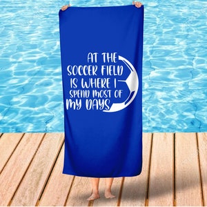 May include: A blue beach towel with a white soccer ball graphic and the text "At the soccer field is where I spend most of my days".