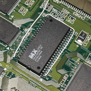 May include: A green printed circuit board featuring a rectangular black integrated circuit chip with the text MX 29LV160TMC-90 2E291100B0 TAIWAN printed in white. The board includes various copper traces, solder points, and electronic components.