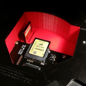Puede incluir: Primer plano de un dispositivo electrónico negro y rojo con una ranura para tarjeta de memoria. Una tarjeta de memoria está insertada en la ranura. El texto en la tarjeta de memoria dice "Kingston 4GB SDHC Class 4". El texto en el dispositivo dice "GOCPU v5.6 2015-08-01".