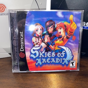 May include: Skies of Arcadia Dreamcast game case. The cover art features three anime-style characters with a blue sky and clouds background. The game case is in a clear plastic case with the Dreamcast logo.