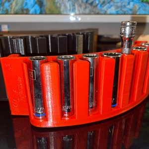 Könnte beinhalten: Ein roter 3D-gedruckter Steckschlüssel-Organizer mit sechs Stecknüssen. Der Organizer hat die Aufschrift "1/4 Drive" auf der Seite. Die Stecknüsse sind silberfarben und haben blaue und rote Markierungen.