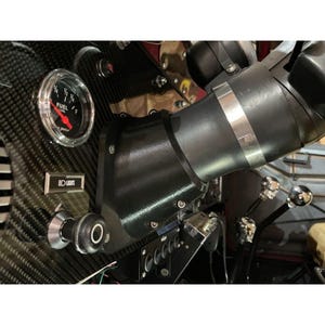 May include: A vehicle dashboard featuring a carbon fibre texture panel, a round fuel gauge with a red needle, a black steering column cover secured with a metal band, and a pull-knob labelled LIGHTS. The assembly includes various switches and levers.