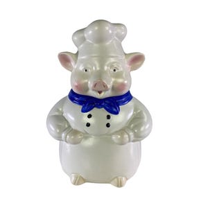 Può includere: Statuina di maiale in ceramica vestita da chef, con cappello e giacca bianchi con bottoni neri. Il maiale ha muso, orecchie e guance rosa e un fazzoletto blu. Un oggetto decorativo per la cucina.
