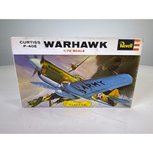 Może przedstawiać: Pudełko z modelem do sklejania Revell samolotu Curtiss P-40E Warhawk w skali 1/72. Pudełko zawiera ilustrację zielono-niebieskiego myśliwca ze słowem ARMY na skrzydle, na tle zachmurzonego nieba, z napisem CURTISS P-40E WARHAWK.