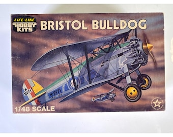 May include: A Life-Like Hobby Kits model airplane box for a Bristol Bulldog. The box features an illustration of a silver biplane with yellow wheels and the text K-2171. The packaging displays the text 1/48 SCALE against a cloudy sky background.