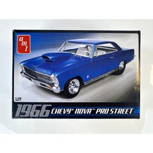 Peut inclure: Une boîte de kit de modèle réduit pour une Chevy Nova Pro Street de 1966, montrant une voiture bleue avec une prise d'air sur le capot, des pare-chocs et des roues chromés. La boîte affiche le logo AMT, l'échelle 1:25 et le texte 1966 CHEVY NOVA PRO STREET.