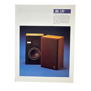 May include: A vintage JBL L19 advertisement featuring two two-way bookshelf speakers with wooden cabinets. One speaker is shown with a black front panel, a woofer, and a tweeter, while the other is covered by a brown grille. Text describes the L19 model.