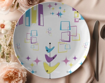 May include: White ceramic dinner plate with a mid-century modern design featuring a stylised tree with yellow, purple, and blue leaves, surrounded by geometric shapes and stars in yellow, blue, and pink.