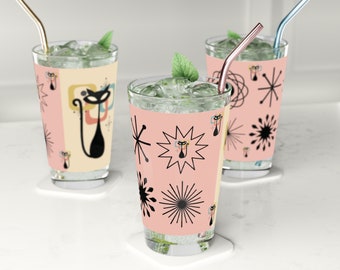 May include: Three clear glass tumblers with pink and black retro cat designs. Each glass has a metal straw and is filled with ice and a clear liquid.