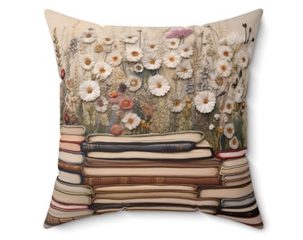 May include: A decorative throw pillow with a beige background featuring a stack of books topped with a cluster of white daisies and other flowers.