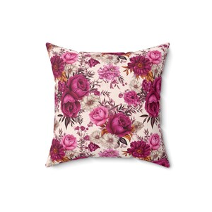 May include: A square throw pillow with a floral pattern. The pillow features a cream background with pink and burgundy roses, leaves, and other flowers.