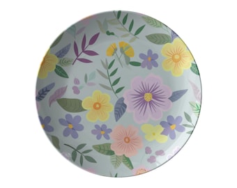 May include: A round, light blue plate with a floral pattern. The design features various flowers in yellow, purple, and pink, along with green leaves and stems. The plate is a decorative item for serving food.