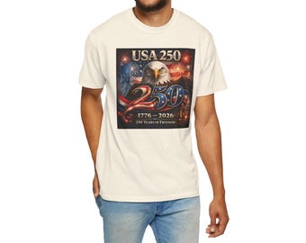 May include: Off-white t-shirt with a commemorative graphic for the 250th anniversary of the USA. The design includes an eagle, fireworks, and the text "USA 250" with the years "1776-2026" and "250 Years of Freedom".