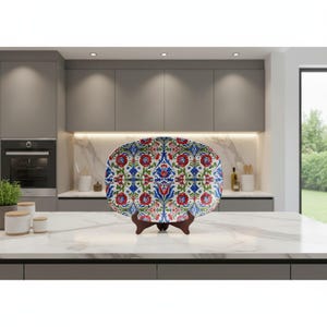 May include: Oval decorative plate with a floral pattern in red, blue, and green on a white background. The plate is displayed on a wooden stand. The plate is a decorative item for the home.