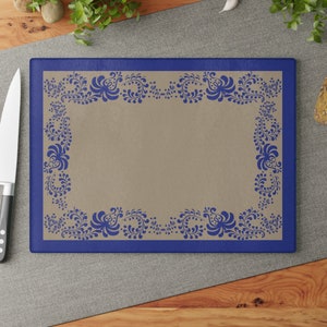 Puede incluir: Una tabla de cortar azul y beige con un borde floral decorativo. El borde está formado por flores y hojas estilizadas azules.