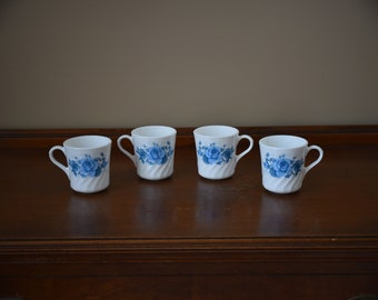 May include: Four white ceramic mugs with blue floral designs. The mugs have a twisted design and a handle on the side.