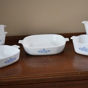 May include: A set of six white ceramic baking dishes with blue floral designs. The dishes are arranged on a wooden surface.
