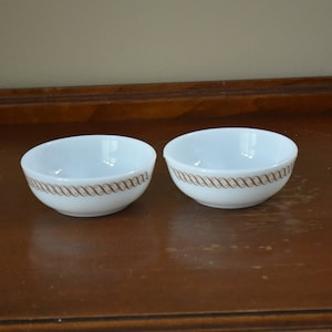 May include: Two white ceramic bowls with a brown swirl design around the rim.