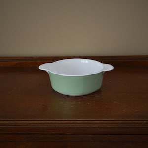 May include: A green and white ceramic baking dish with two handles. The dish is sitting on a wooden surface.