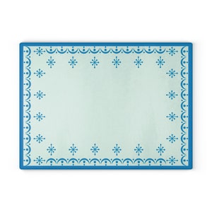 May include: Rectangular cutting board with a light blue center and a dark blue border. The border features a repeating pattern of snowflakes and dots. The cutting board is designed for kitchen use.