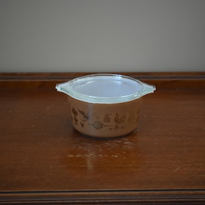 May include: A brown glass baking dish with a clear glass lid. The dish has a gold design of birds and other animals.