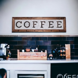 May include: A wooden sign with the word "COFFEE" in white letters on a white background. The sign is hanging above a counter with a wooden crate and other items.