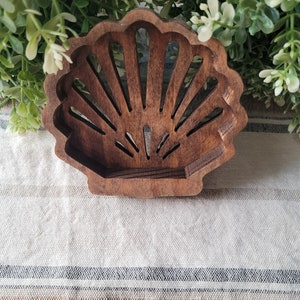 May include: A wooden seashell-shaped decorative object with a cutout design. The seashell is brown and has a natural wood finish.