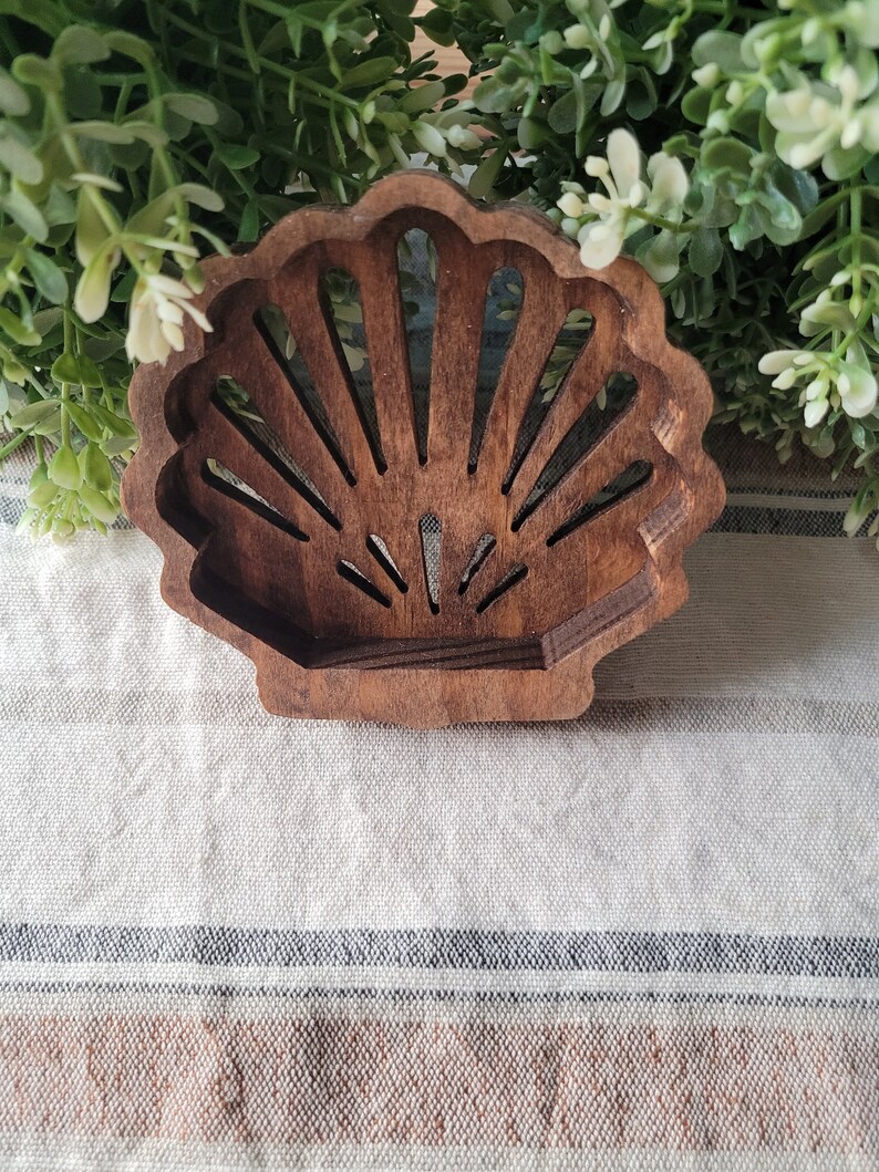 May include: A wooden seashell-shaped decorative object with a cutout design. The seashell is brown and has a natural wood finish.