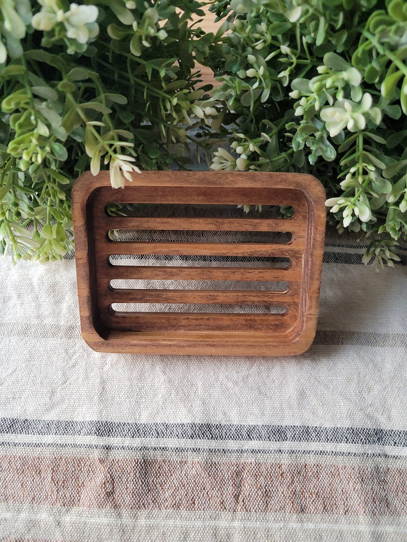 May include: A wooden soap dish with a slatted design. The dish is made of dark brown wood and has a rectangular shape.