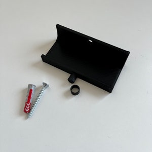 Peut inclure: Un support mural en plastique noir avec une vis, une cheville en plastique et un anneau en caoutchouc noir. Le support mural est con&ccedil;u pour tenir un petit objet, comme un t&eacute;l&eacute;phone ou une tablette.